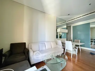 Modern living room with stylish furniture and dining area, featuring sleek glass table and wooden flooring.
