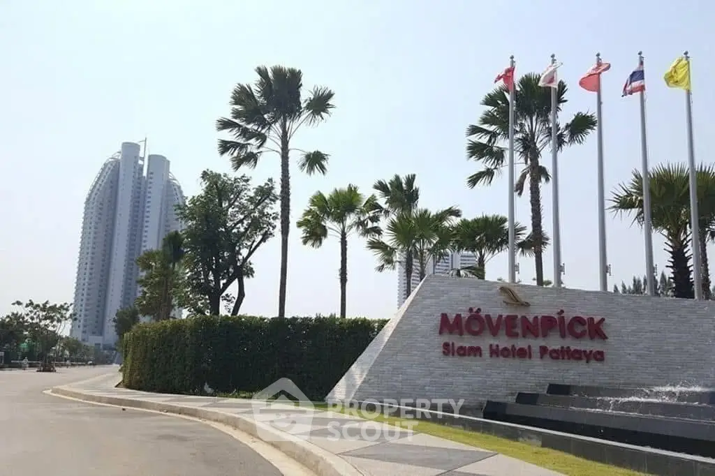 Luxurious hotel entrance with palm trees and flags in Pattaya, showcasing modern architecture.