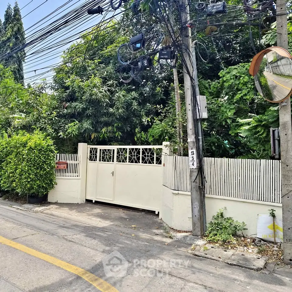 Charming residential entrance with lush greenery and secure gate in a serene neighborhood.
