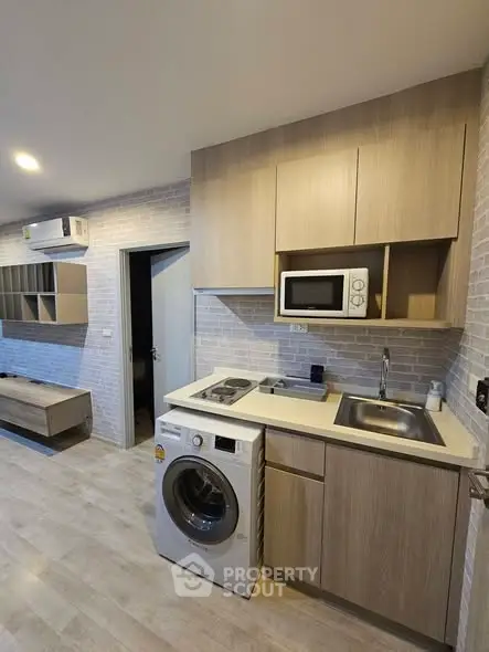 Modern compact kitchen with washing machine and microwave in stylish apartment.