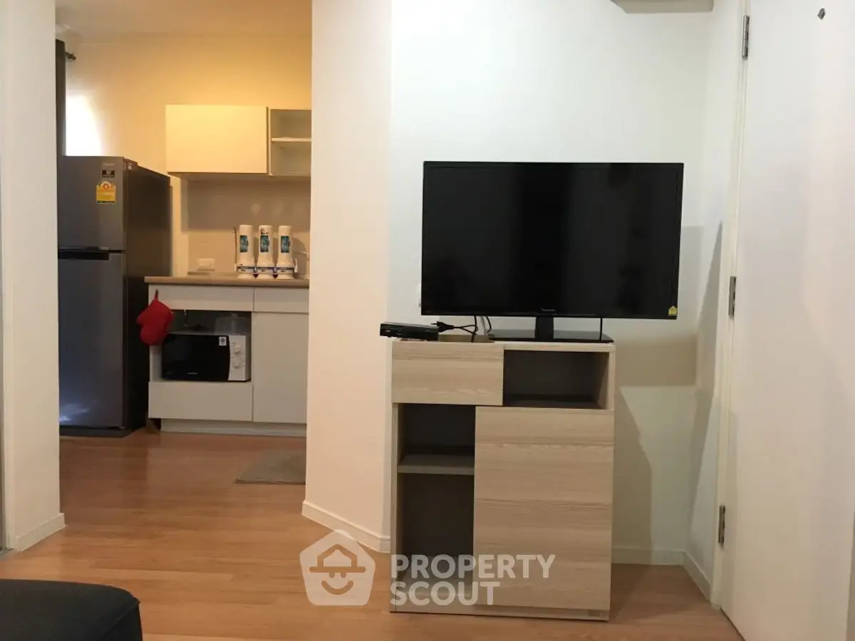 Modern apartment interior with compact kitchen and cozy living area featuring a flat-screen TV.
