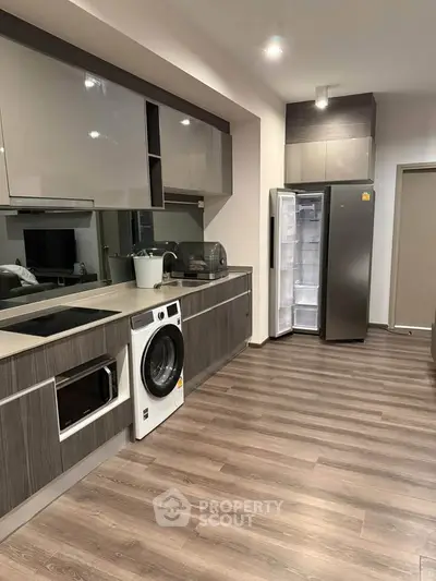 Modern kitchen with sleek appliances and wood flooring, featuring a washing machine and open fridge.