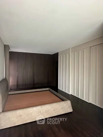 Spacious modern bedroom with sleek dark wood flooring and built-in wardrobe.