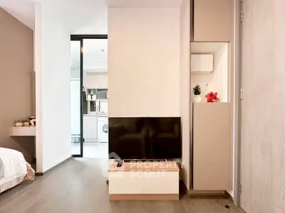 Modern apartment interior with sleek TV setup and view into kitchen with washing machine.