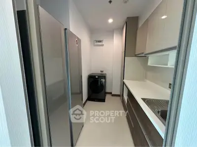 Modern kitchen with sleek cabinetry and appliances, featuring a washing machine and spacious fridge.