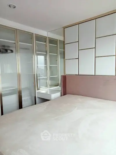 Modern bedroom with sleek glass wardrobe and stylish headboard in a contemporary apartment.