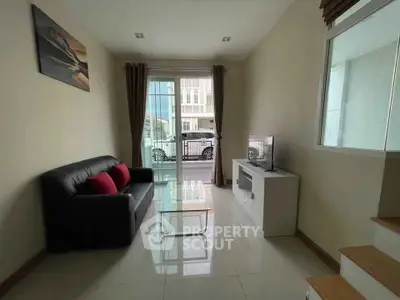 Cozy living room with modern decor, featuring a sleek black sofa, glass coffee table, and a TV unit near large windows.