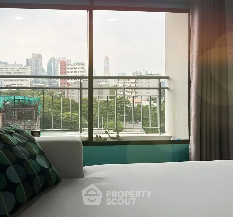 Modern bedroom with city view through large window, featuring stylish decor and comfortable bedding.