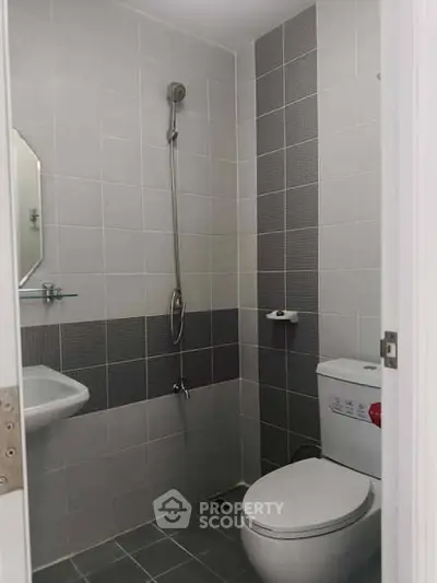 Compact modern bathroom with shower, toilet, and sink in sleek tile design.