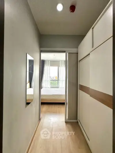 Modern apartment hallway leading to a bright bedroom with large windows and stylish decor.