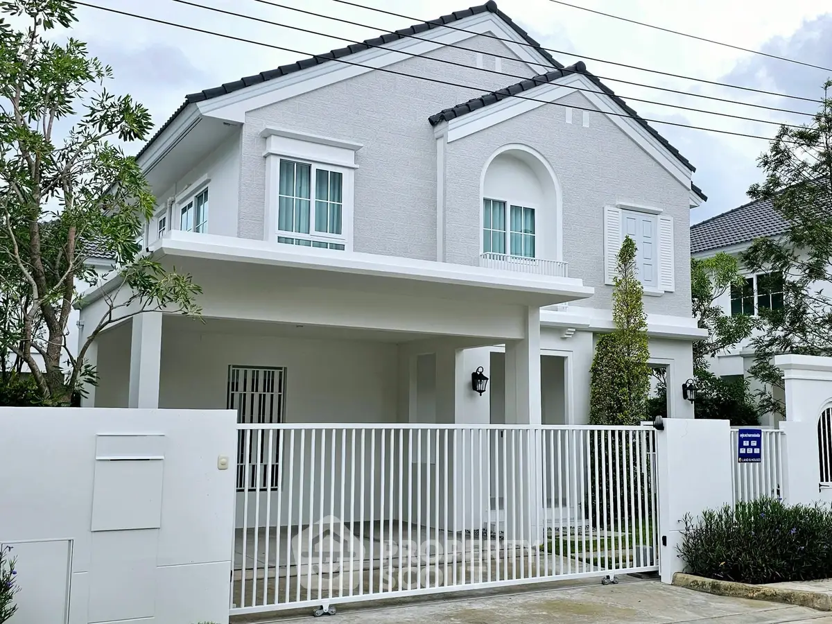 Elegant two-story white house with gated entrance and lush greenery.