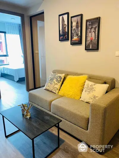 Cozy modern living room with comfortable sofa adorned with vibrant cushions, sleek coffee table, and elegant wall art, leading to a well-lit bedroom.