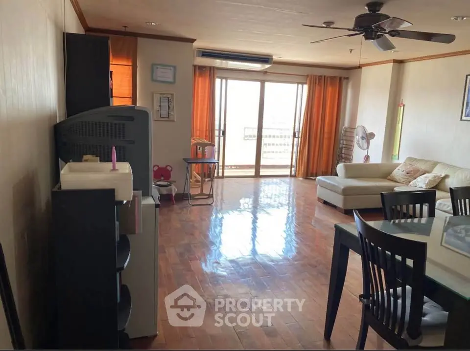 Spacious living room with wooden flooring and large windows leading to a balcony.