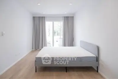 Spacious minimalist bedroom with large window and modern bed frame, perfect for serene living.