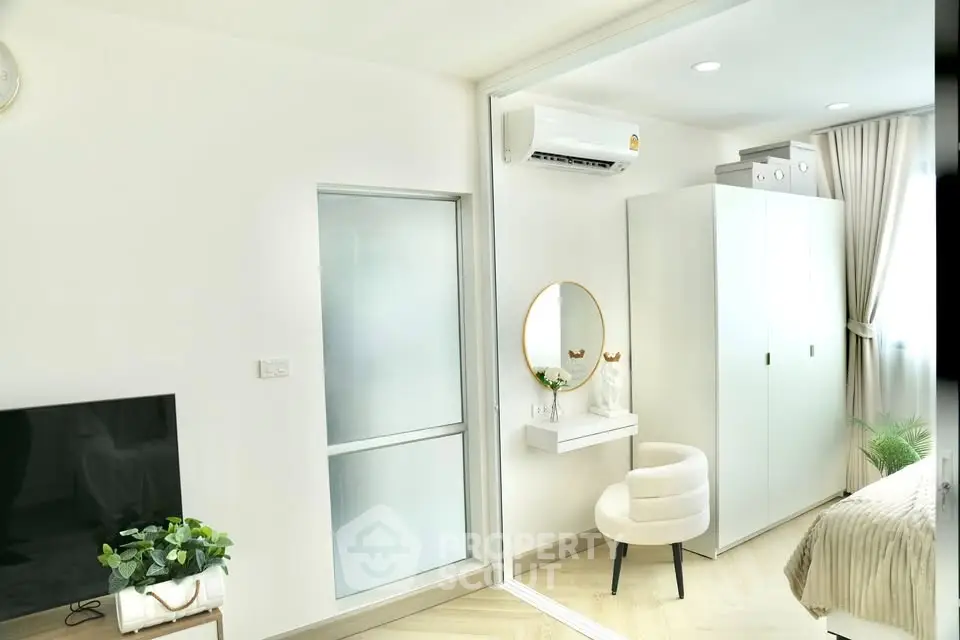 Modern bedroom with sleek white furniture and air conditioning, featuring a cozy chair and stylish decor.