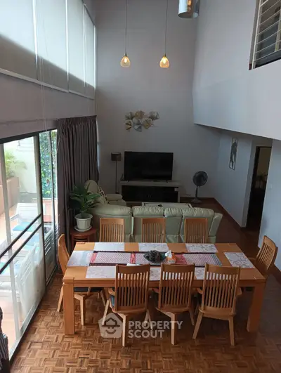 Spacious living room with high ceiling and elegant dining area, featuring modern decor and natural light.