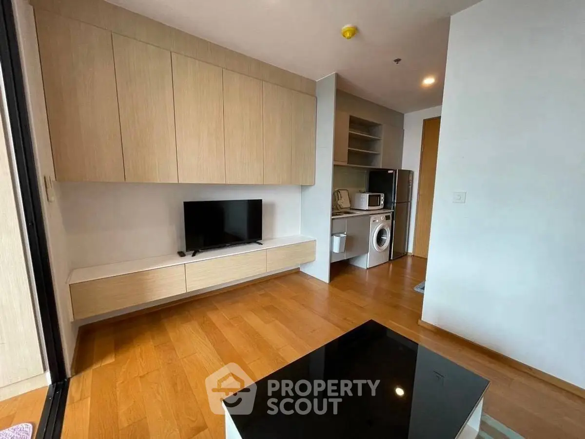 Modern living room with built-in cabinets and appliances, featuring wooden flooring and sleek design.