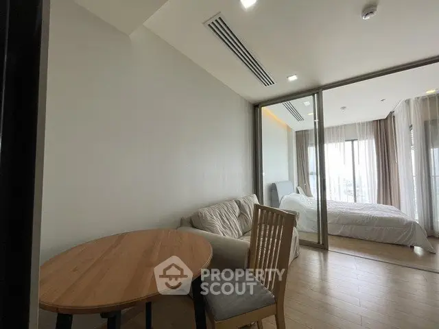 Modern apartment interior with cozy living area and bedroom separated by glass partition.
