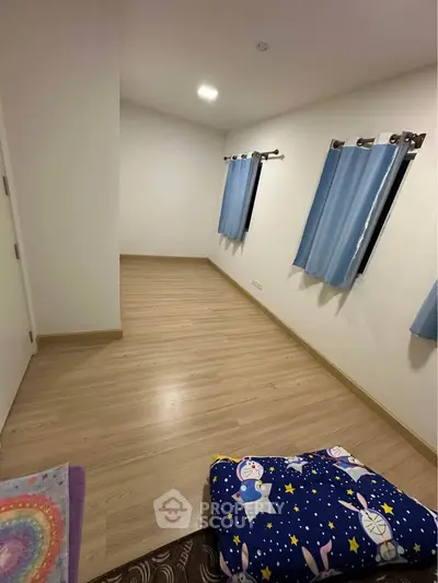 Spacious empty room with wooden flooring and blue curtains, ideal for customization.