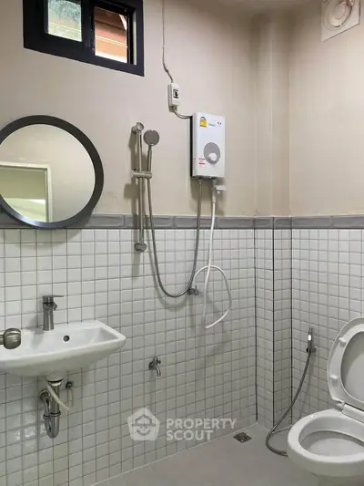 Modern bathroom with white tiles, round mirror, and electric shower heater.