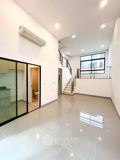 Spacious modern living room with high ceilings and mezzanine, featuring sleek tile flooring and large windows.