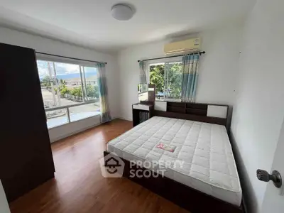 Bright bedroom with large windows and wooden flooring, featuring a double bed and air conditioning.