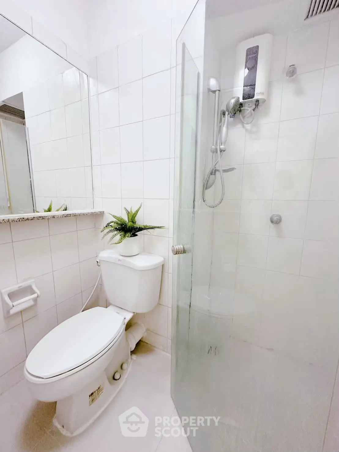 Compact bathroom with shower and toilet, featuring white tiles and a small plant for a fresh look.
