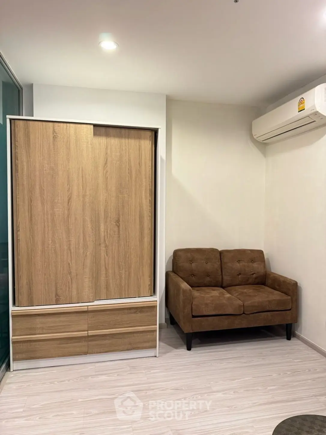 Modern living room with sleek wooden wardrobe and cozy brown sofa, featuring minimalist design and air conditioning.