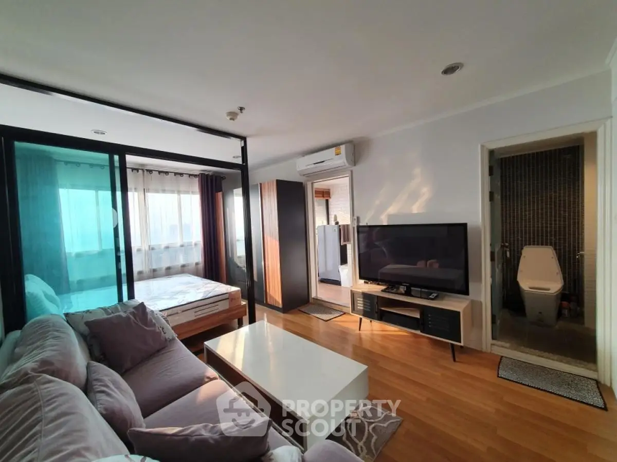 Modern apartment interior with cozy living room and bedroom, featuring wooden flooring and large TV.