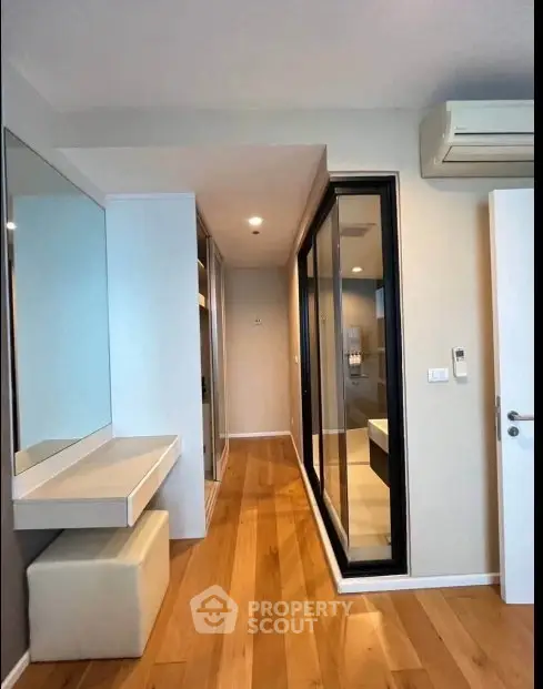 Modern apartment hallway with wooden flooring and mirrored closet doors.