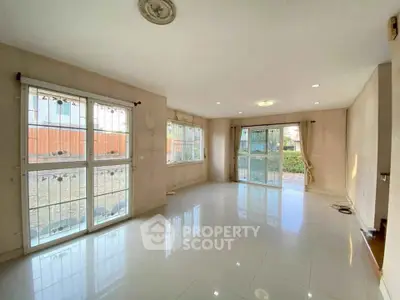 Spacious living room with large windows and glossy tile flooring, offering abundant natural light.