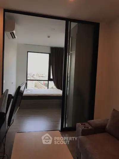 Modern apartment with sleek wooden flooring leading to a sunlit balcony offering a cityscape view, perfect for urban living.