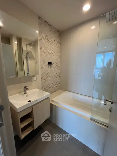 Modern bathroom with stylish tile accent wall and glass-enclosed bathtub.
