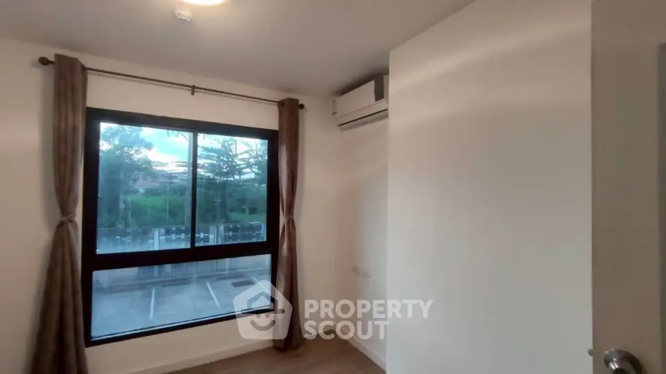 Bright room with large window and air conditioning, overlooking parking area.