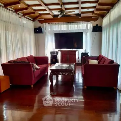 Spacious living room with elegant wooden flooring and plush red sofas, perfect for relaxation and entertainment.