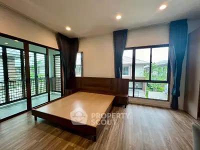 Spacious bedroom with large windows and wooden flooring in modern home.