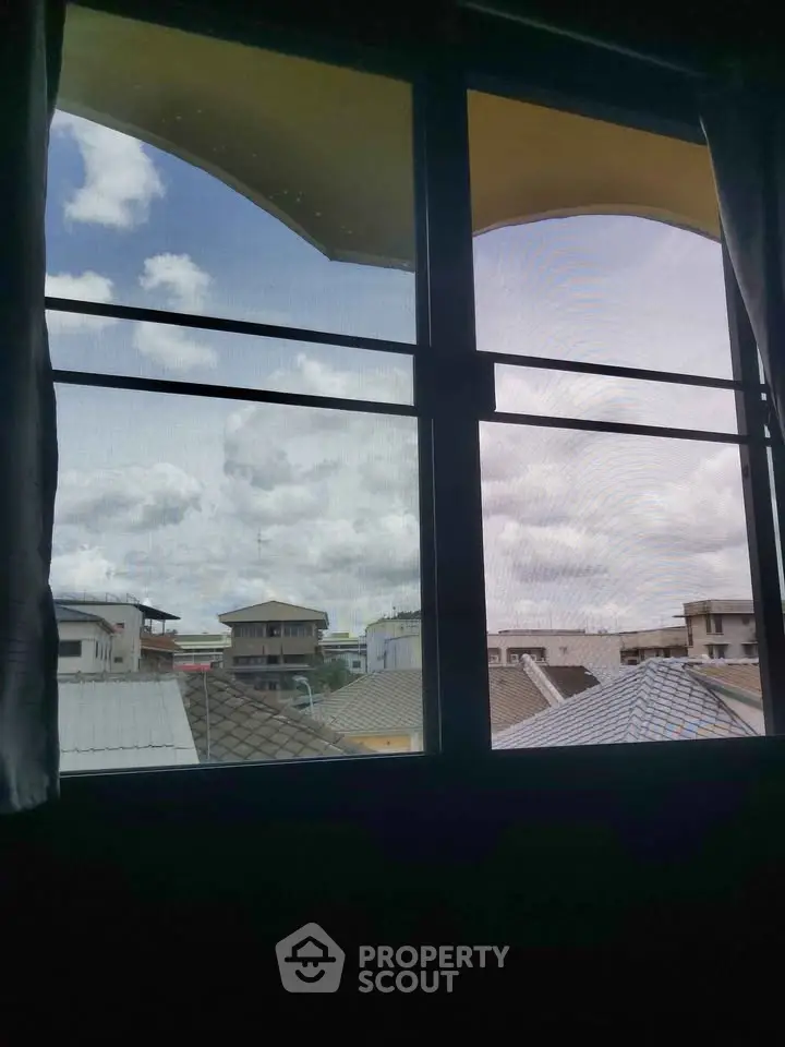 Scenic view from a window showcasing rooftops and a cloudy sky.
