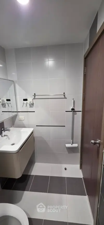 Modern bathroom with sleek design and neutral tiles, featuring a wall-mounted sink and shower area.