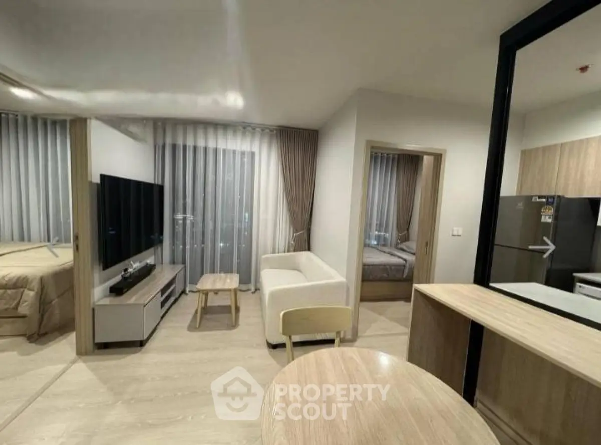 Modern open-plan living room with sleek furniture and large TV, adjacent to a cozy bedroom.