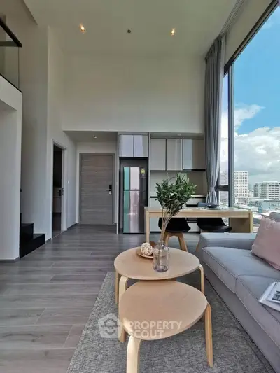 Modern living room with high ceilings and city view, featuring stylish furniture and large windows.