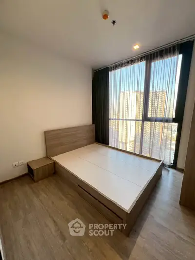 Spacious bedroom with large windows offering city views in modern apartment.