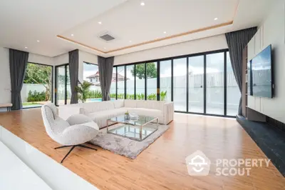 Spacious modern living room with large windows and pool view, featuring elegant furniture and wooden flooring.