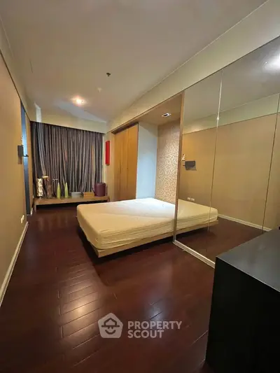 Modern bedroom with wooden flooring and mirrored closet doors in a stylish apartment.
