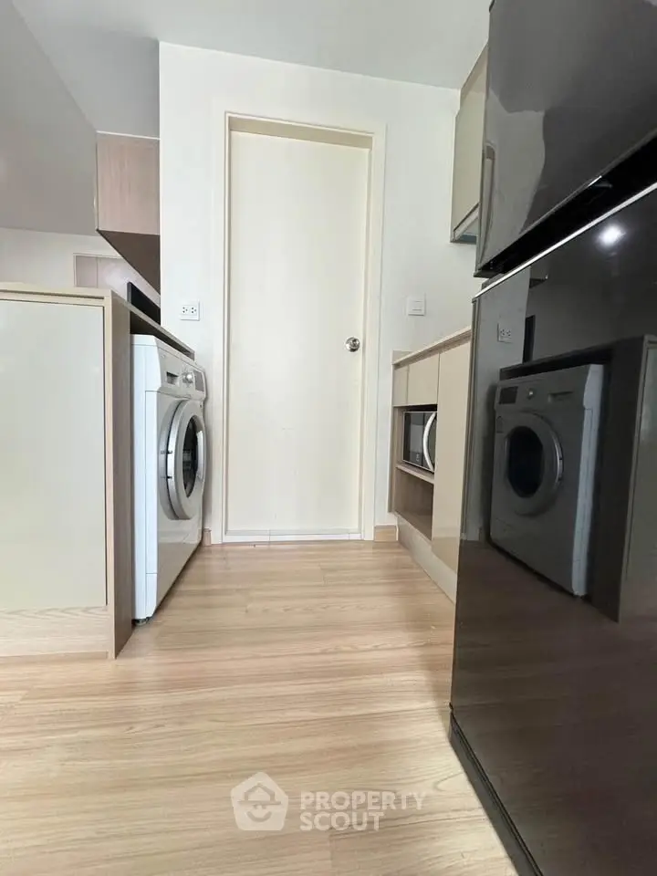 Modern kitchen with sleek appliances and washing machine, featuring light wood flooring.