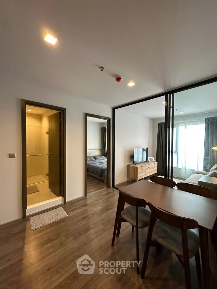 Modern apartment interior with open living and dining area, featuring glass partition and stylish furnishings.
