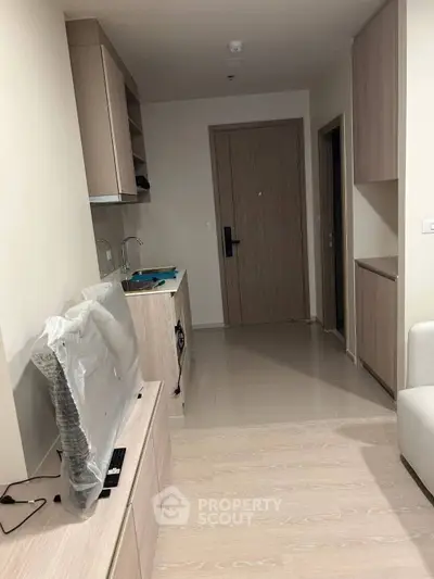 Modern apartment interior with compact kitchen and living area, featuring sleek cabinetry and a new TV.