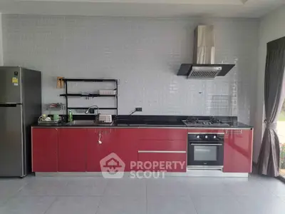 Modern kitchen with sleek red cabinets, gas stove, and stainless steel appliances.