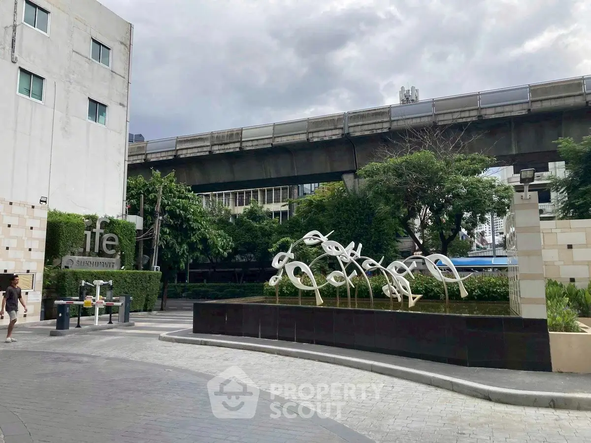 Modern urban building entrance with artistic sculpture and lush greenery
