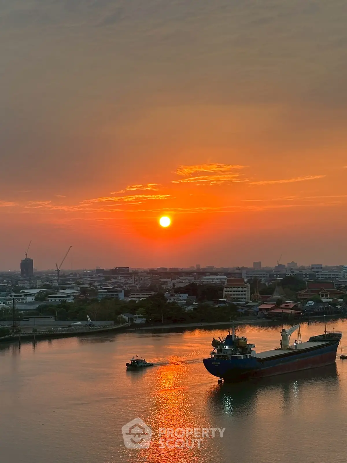 Stunning sunset view over a cityscape with a river and ships, perfect for waterfront property listings.
