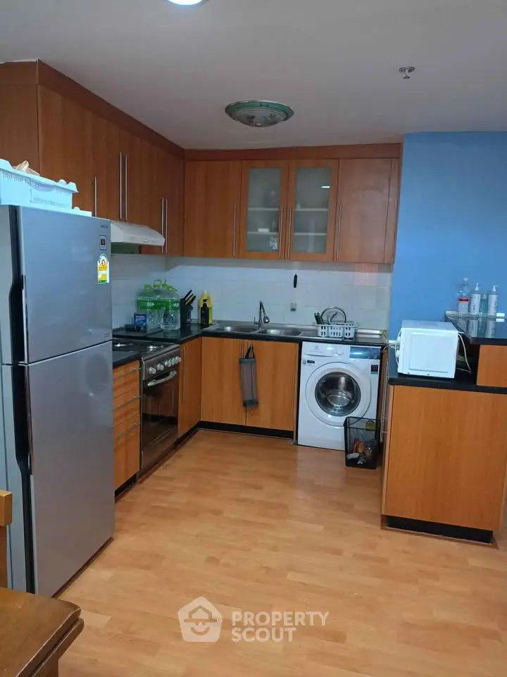 Modern kitchen with wooden cabinets, stainless steel appliances, and washing machine.